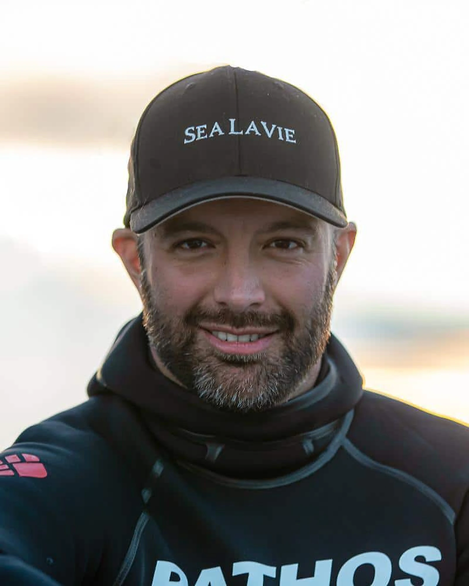 John Kowitz in a wetsuit and cap, photographed at golden hour on the water